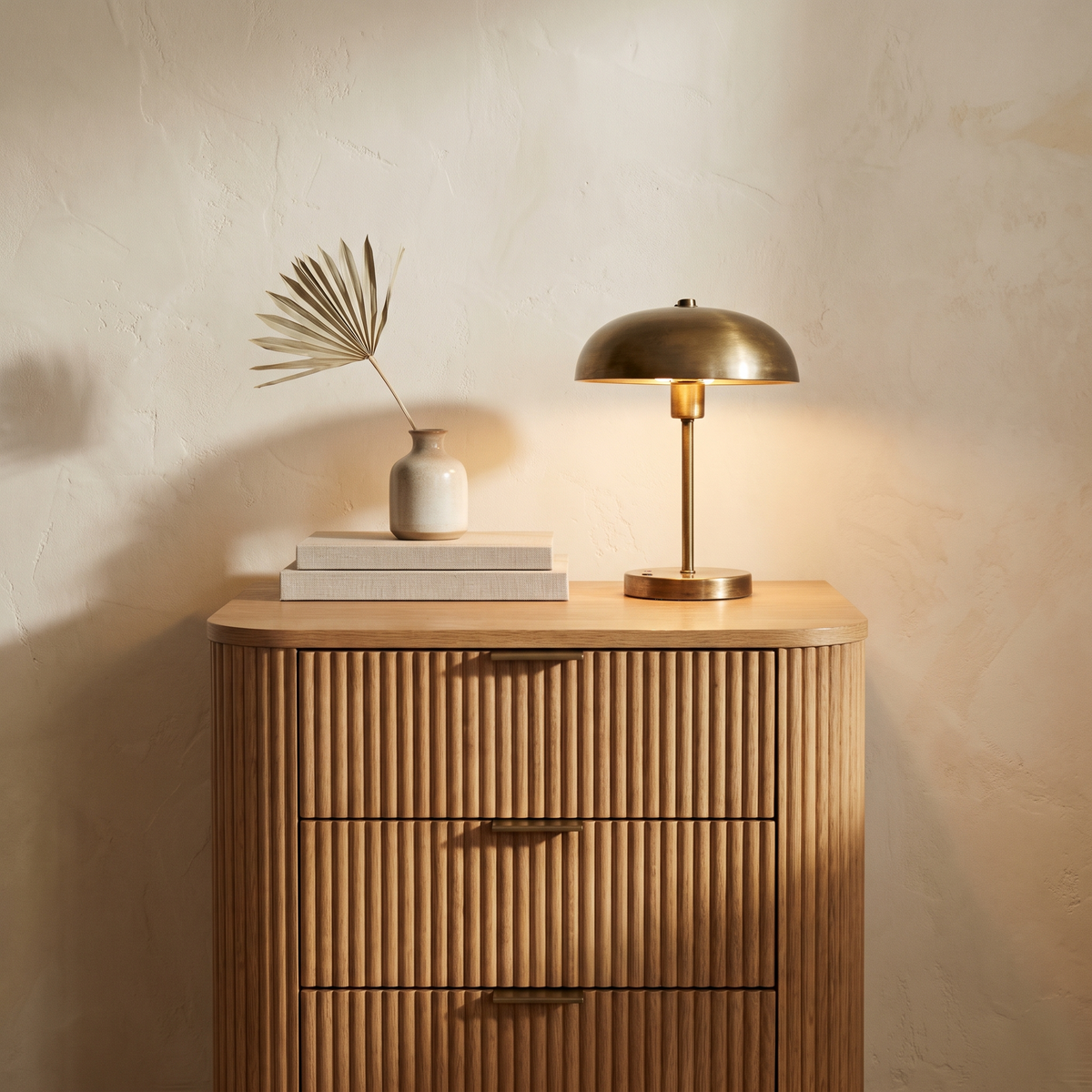 Fluted oak nightstand with a brass lamp and books